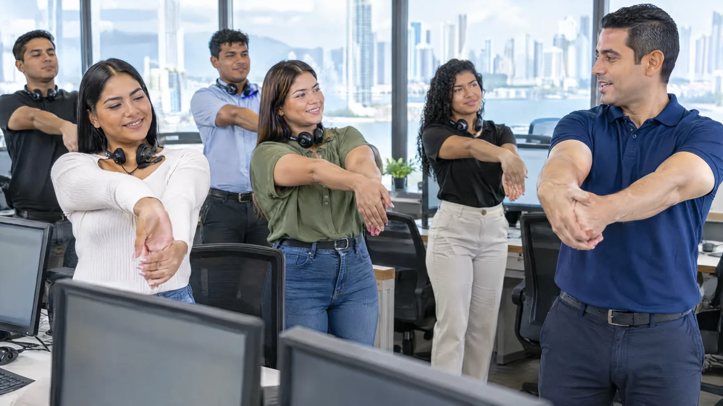 Office team stretching wrists and forearms guided by a THA instructor